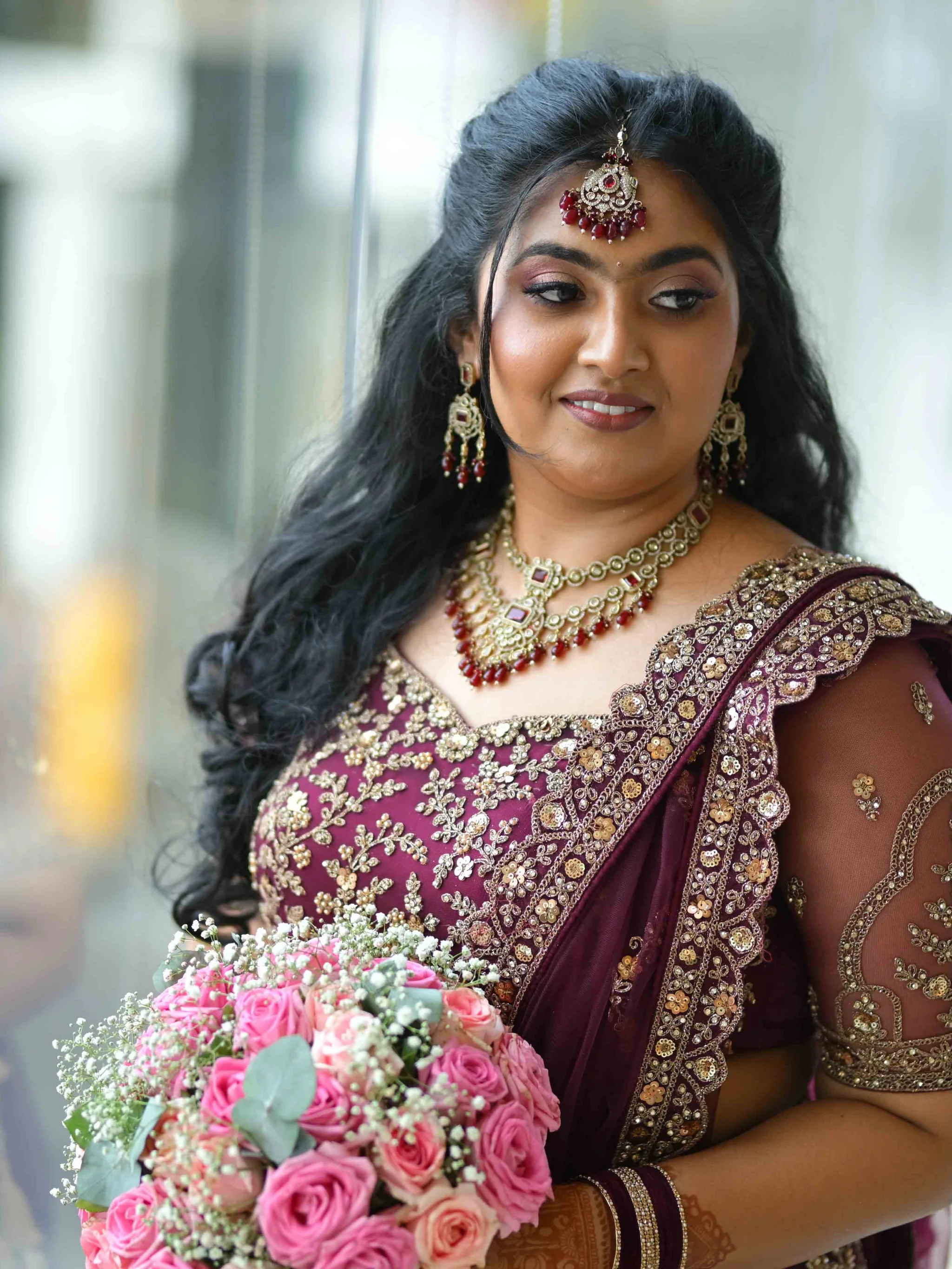 Bridal look in a red lehenga, holding a bouquet of pink roses.
