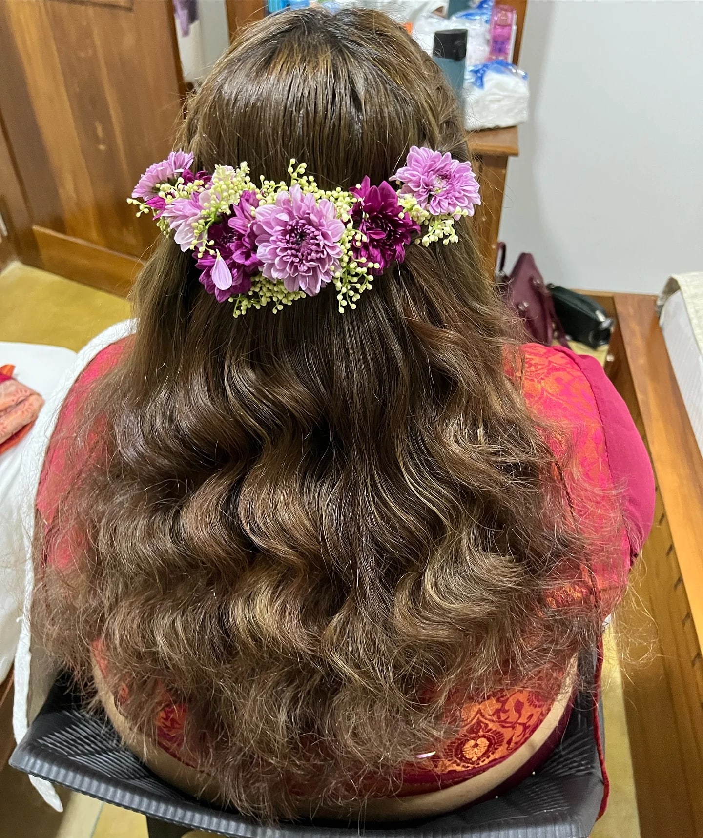 Long waved hair dressed with a lilac and white floral piece, seen from behind.