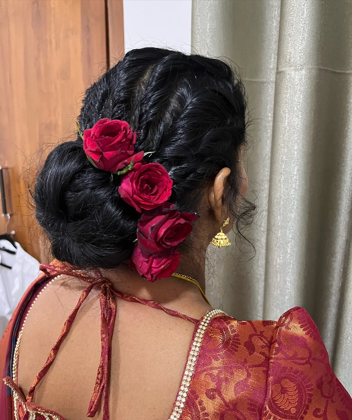 Braided updo finished with red roses, seen from behind.