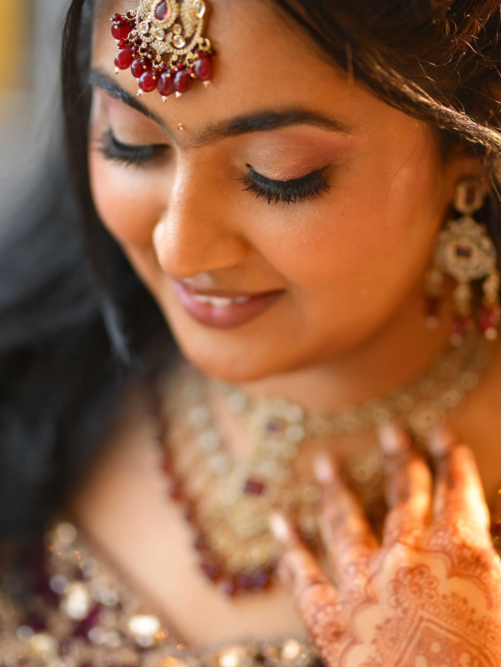 Makeup detail showing blended eyeshadow, lashes and a gold and ruby maang tikka.