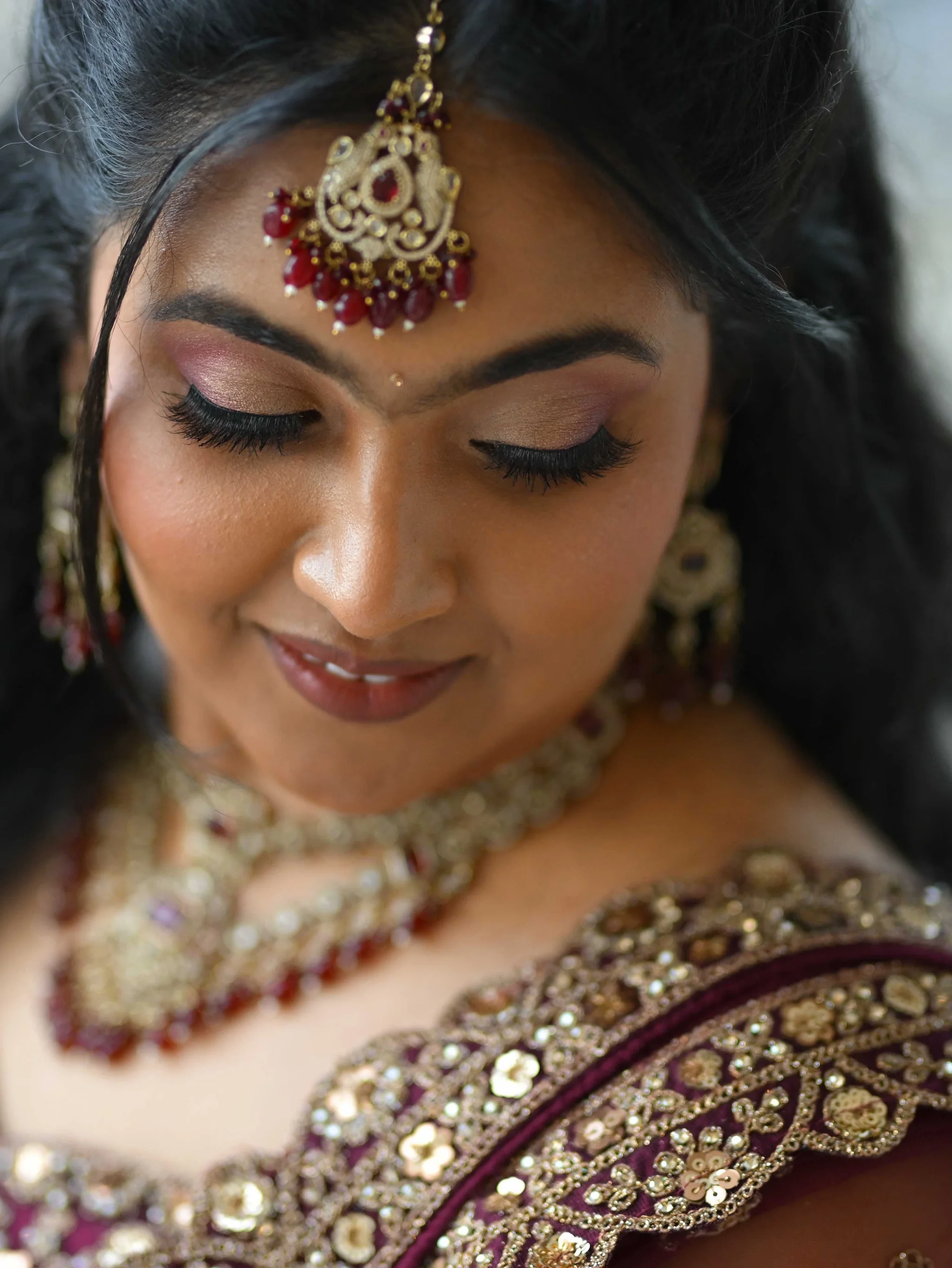 Bridal makeup in close view, with blended warm eyeshadow, defined lashes and a gold maang tikka.