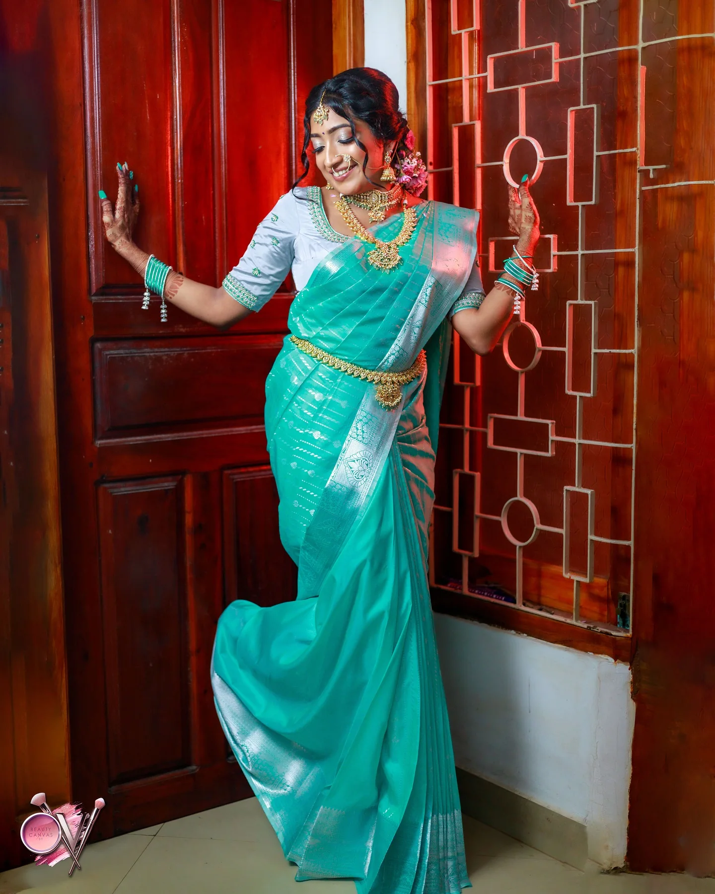 Full-length teal Kanjivaram drape showing the pleats and pallu, beside a carved wooden door.